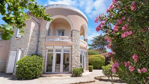 Une maison avec une façade en pierre, un balcon circulaire et une allée gravillonnée.