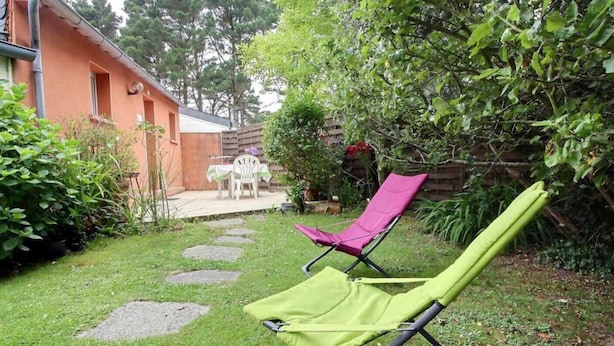 Un jardin avec une terrasse, deux chaises longues et une table avec des chaises.
