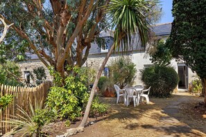 A garden with a table and chairs, a wooden fence, and a stone wall. - Holiday Home 'Maison Ty Bihan' with Private Terrace, Private Garden and Wi-Fi (Lannion)