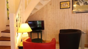 Un escalier menant à un espace de vie comprenant un téléviseur, une lampe et un fauteuil rouge.