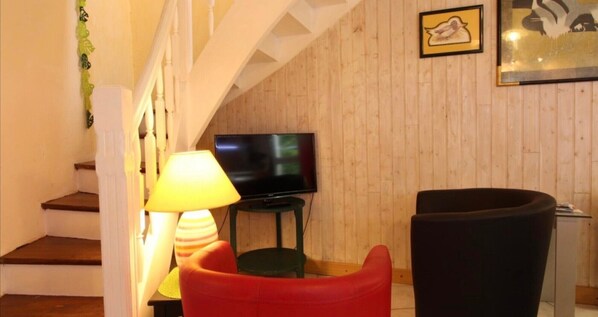 Een trap die leidt naar een woonruimte met een televisie, een lamp en een rode stoel.