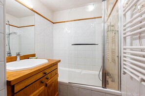 A bathroom with a wooden vanity, a glass shower enclosure, and a white tiled wall. - Apartment 'Appartement Résidence Ours Blanc' with Mountain View, Shared Terrace and Wi-Fi (Les Houches)