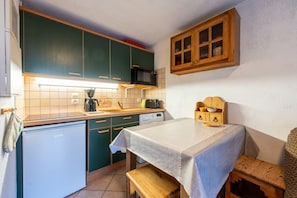 Een kleine keuken met groene kastjes, een magnetron, een broodrooster en een houten kastje boven de gootsteen.