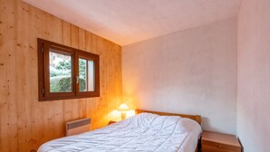 Ein Schlafzimmer mit Holzwänden, einem Fenster, einem Bett, einem Nachttisch und einer Lampe.