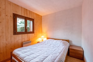 Une chambre avec des murs en bois, une fenêtre, un lit, une table de chevet et une lampe.