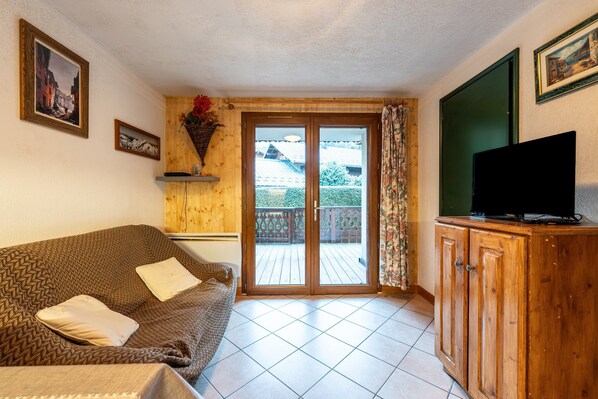 A living room with a sofa, a television on a wooden cabinet, and a sliding glass door leading to an outdoor area. - Apartment 'Appartement Résidence Ours Blanc' with Mountain View, Shared Terrace and Wi-Fi (Les Houches)