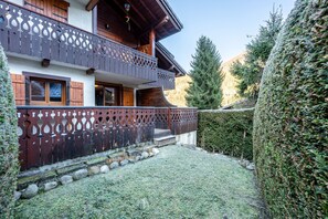 A two-story wooden building with balconies, a wooden fence, and a well-maintained garden with rocks and hedges.