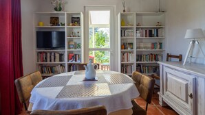 Een gezellige woonkamer met een ronde tafel, stoelen, een boekenkast, een televisie en een raam met uitzicht op groen.