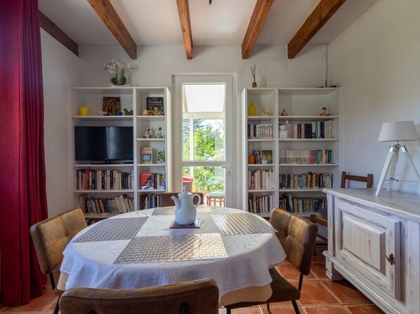 Una sala de estar acogedora con una mesa redonda, sillas, una estantería, un televisor y una ventana con vistas a la vegetación.