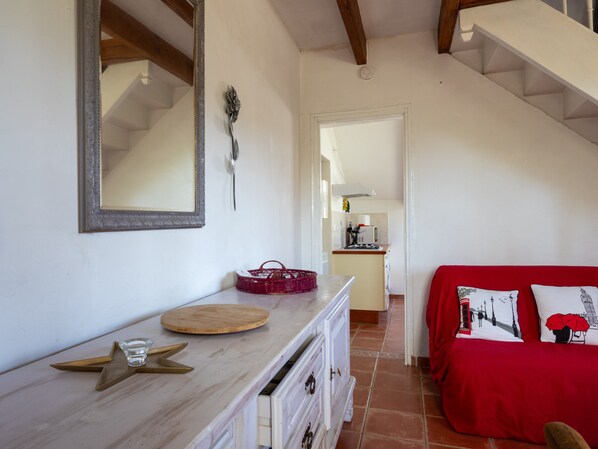 Une pièce comprenant une commode en bois, un canapé rouge, un miroir et un escalier menant à une autre pièce.