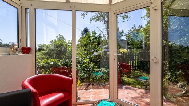 Een conservatorium met een rode stoel, een kleine tafel met een boek, en uitzicht op de tuin.