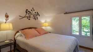 Een slaapkamer met een bed, twee bedlampen, een kunstwerk aan de muur en een raam met uitzicht op groen.