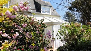 Una casa con facciata bianca, una finestra visibile e un giardino con piante fiorite.