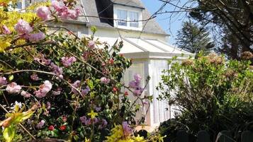 A house with a white exterior, a visible window, and a garden with flowering plants.