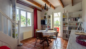 Een kamer met een eettafel, stoelen, een boekenkast, een radiator en een raam met gordijnen.