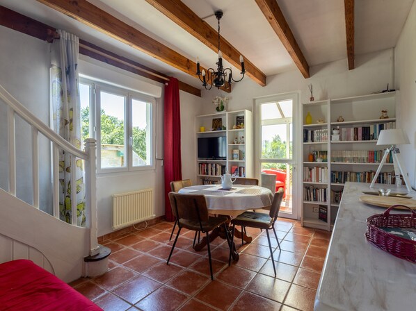 Une pièce comprenant une table à manger, des chaises, une bibliothèque, un radiateur et une fenêtre avec des rideaux.