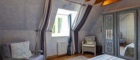 A bedroom with a bed, a chair, a dresser, and a window with curtains.