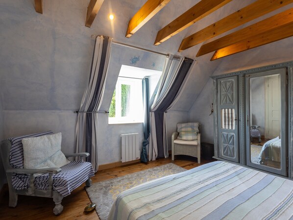 Een slaapkamer met een bed, een stoel, een dressoir en een raam met gordijnen.
