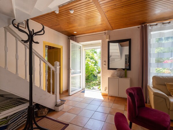 A room with a wooden ceiling, a staircase, a red chair, a white sofa, and a view of greenery outside.