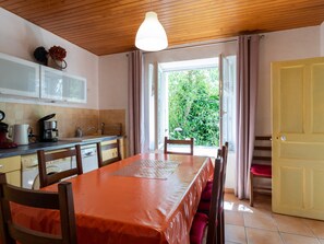 Une cuisine équipée d’une table à manger, de chaises, d’une machine à café et d’une fenêtre avec des rideaux.