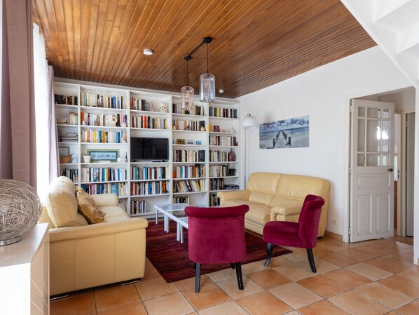 Een woonkamer met een beige bank, een rode stoel, een boekenkast, een televisie en een houten plafond.