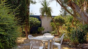 Un patio al aire libre con una mesa y sillas, rodeado de plantas y árboles.