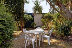 An outdoor patio with a table and chairs, surrounded by various plants and trees.