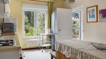 A bedroom with a bed, a window with a view of greenery, a radiator, and a small table with a lamp.