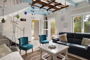 A spacious living area with a black leather sofa, two blue armchairs, a white coffee table, and a wooden ceiling structure.