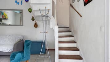 Eine Treppe mit Holzdielen und weißen Wänden, ein blauer Stuhl, ein Metallständers für Kleidung und ein Spiegel an der Wand.