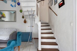 Una escalera con escalones de madera y paredes blancas, una silla azul, un perchero metálico y un espejo en la pared.