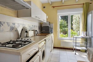 Una cocina con estufa a gas, microondas, hervidor de agua y ventana con vista a follaje.
