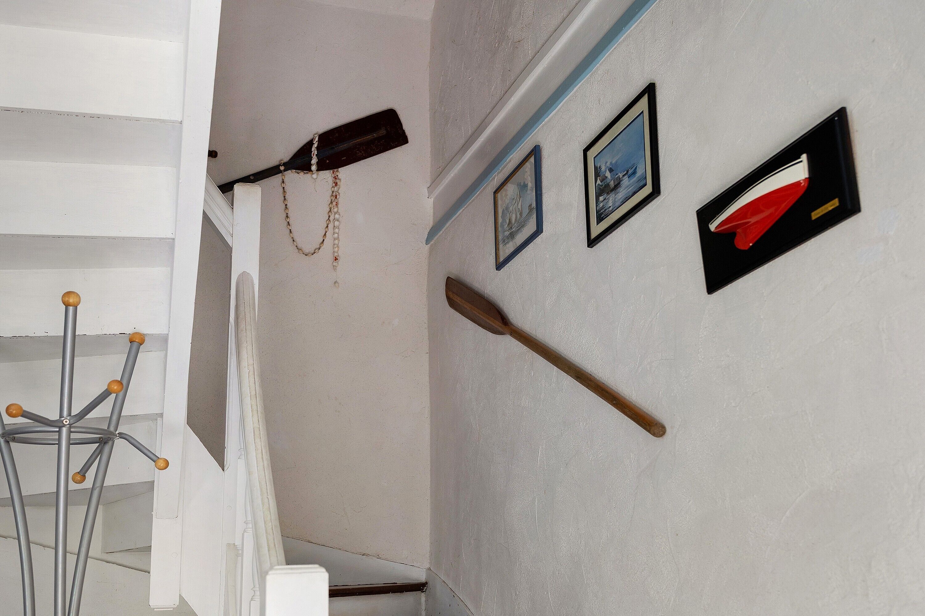 Uma escadaria com corrimão, uma parede com quadros e um cabideiro com casaco e chapéu.
