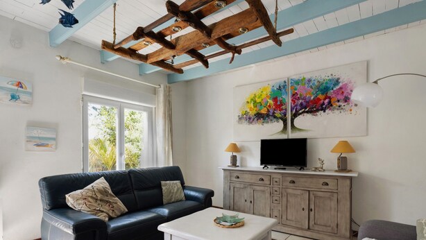 A living room with a black leather sofa, a white coffee table, a television on a wooden cabinet, and a colorful abstract painting on the wall.