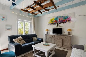 A living room with a black leather sofa, a white coffee table, a television on a wooden cabinet, and a colorful abstract painting on the wall.