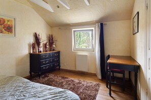 Un dormitorio con cama, cómoda, escritorio, ventana y radiador.