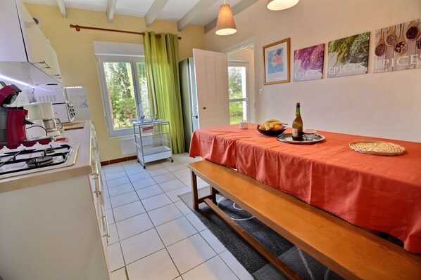 Een kamer met een bed, een tafel met een fles en fruit, een raam met gordijnen en een keukenhoek met apparatuur.