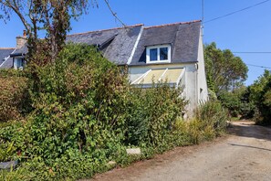 A residential house with a sloped roof, a visible window, and a pathway leading to the entrance.