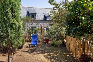 Un patio trasero cercado con una silla azul, una valla de madera y una casa con techo inclinado.