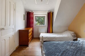 Una habitación pequeña y estrecha con un aparador de madera, una cama con colcha y una ventana con cortinas.