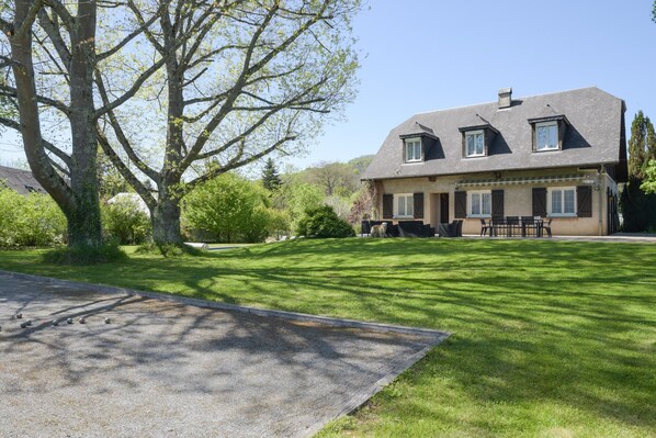 A two-story house with a sloped roof, a front lawn, and a large tree.