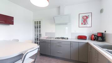 A modern kitchen with a dining table, chairs, a red toaster, a coffee maker, and a framed picture on the wall.