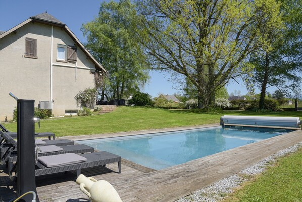 Une piscine avec des chaises longues, une terrasse en bois et une maison en arrière-plan.