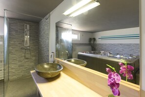 A modern bathroom with a glass shower enclosure, a large mirror, and a wooden vanity with two sinks.