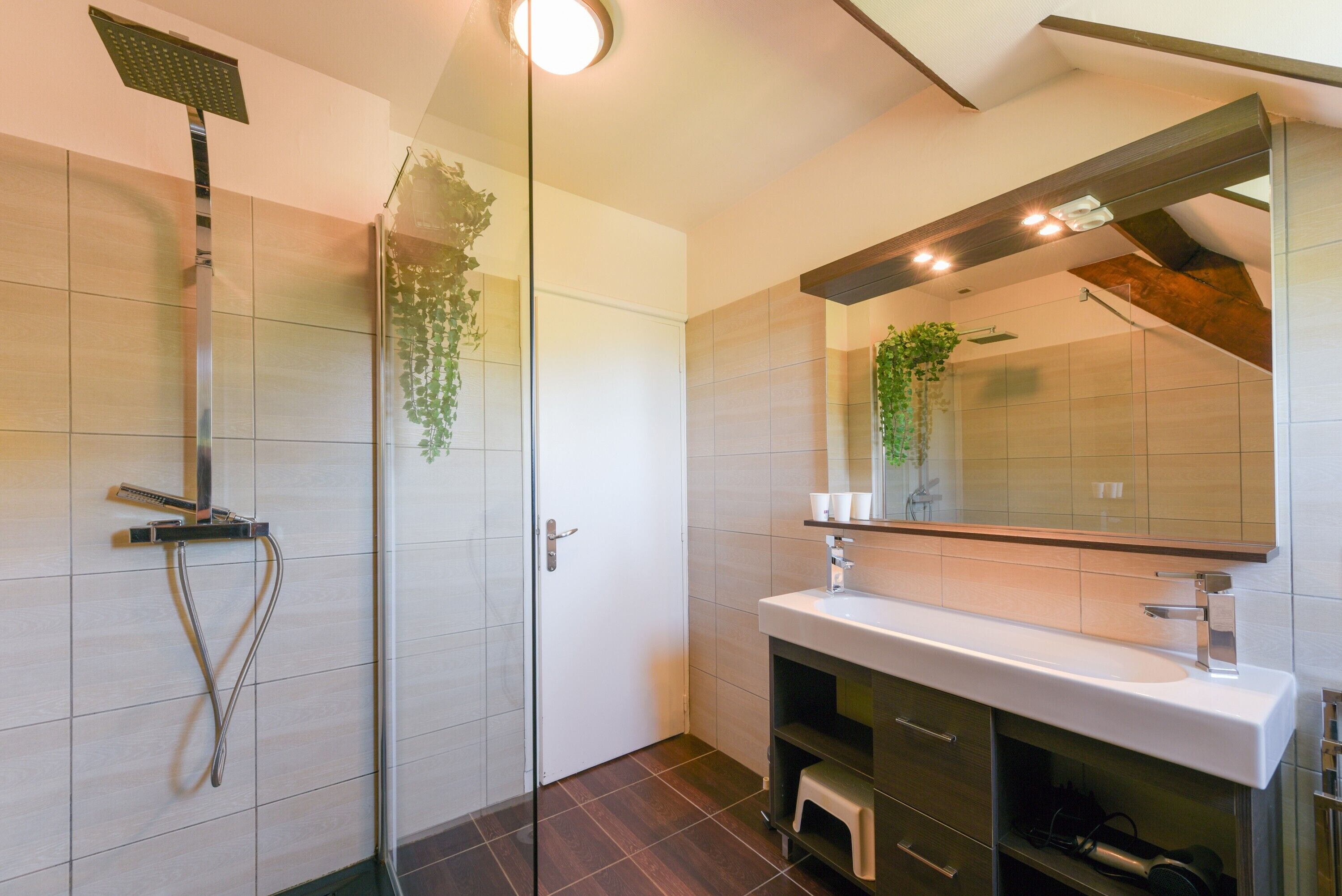 Een moderne badkamer met een douchecabine van glas, een witte wastafel en een grote spiegel.