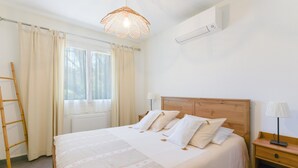 Un dormitorio con cama de madera, ropa de cama blanca, una mesita de noche con lámpara, una ventana con cortinas y un aplique de techo.
