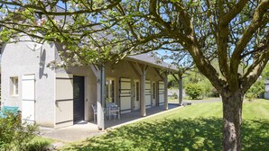 A two-story building with a covered porch, a tree in the foreground, and a grassy lawn.