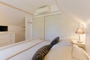 A bedroom with a bed, a TV, a white dresser, a lamp, and a white brick wall.