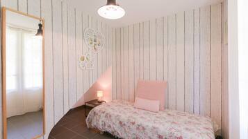 Een slaapkamer met een wand van houten latten, een bed met bloemenbeddengoed, een nachtkastje met een lamp en een spiegel.