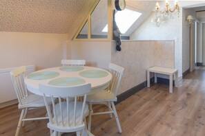 A room with a round table, white chairs, a small bench, a chandelier, and a sloped ceiling with a skylight.